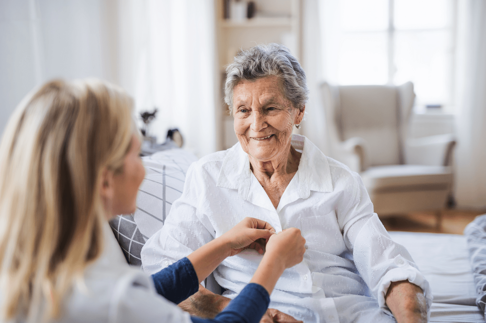 Caregiver helping an older woman button a shirt during dressing support.