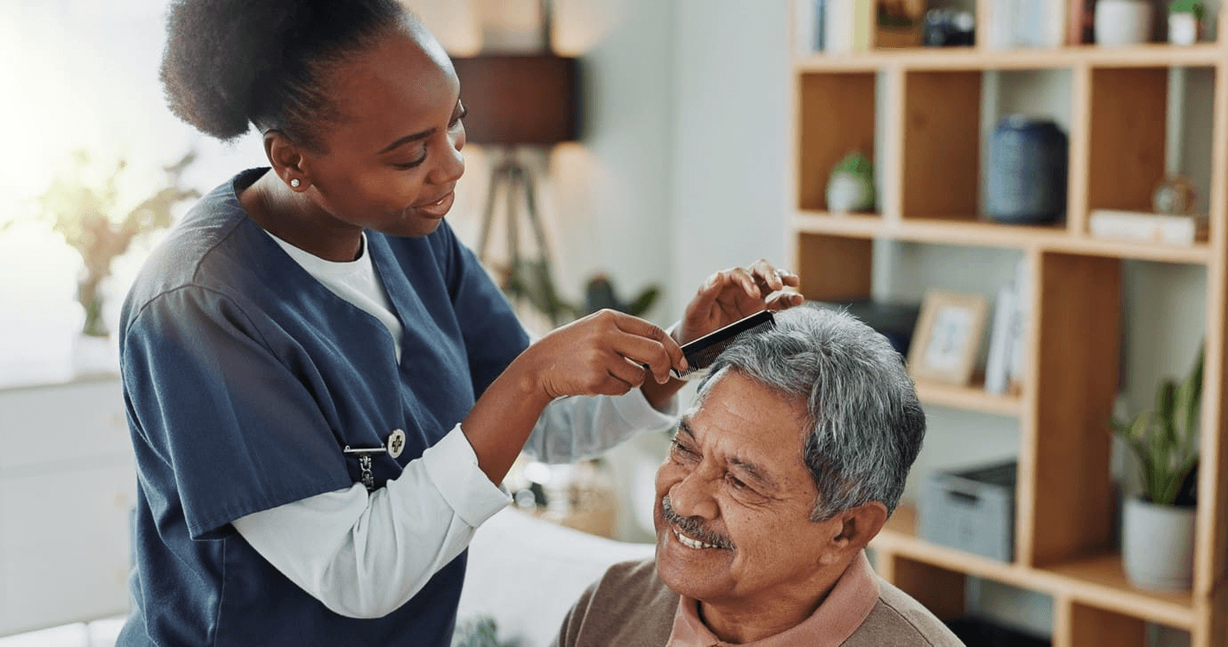 Caregiver gently combing an older man’s hair.